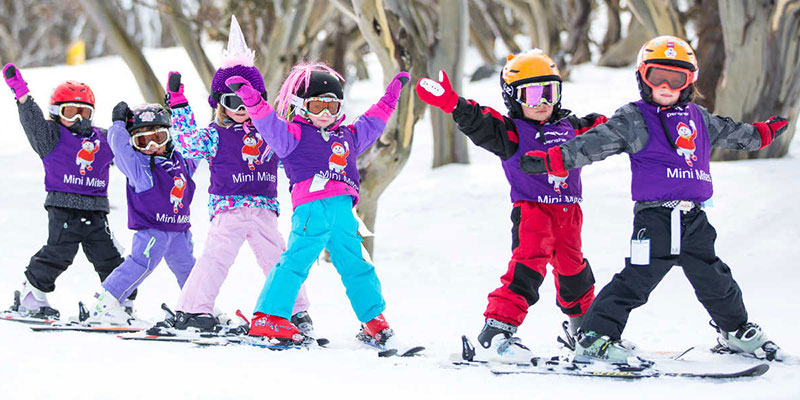 Six kids wearing purple vests in a row on skis.