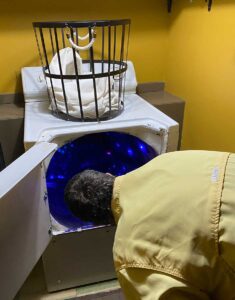 A man peers into the washing machine leading into the sparkling blue unknown at Meow Wolf. Photo by Cheryl Fallstead.